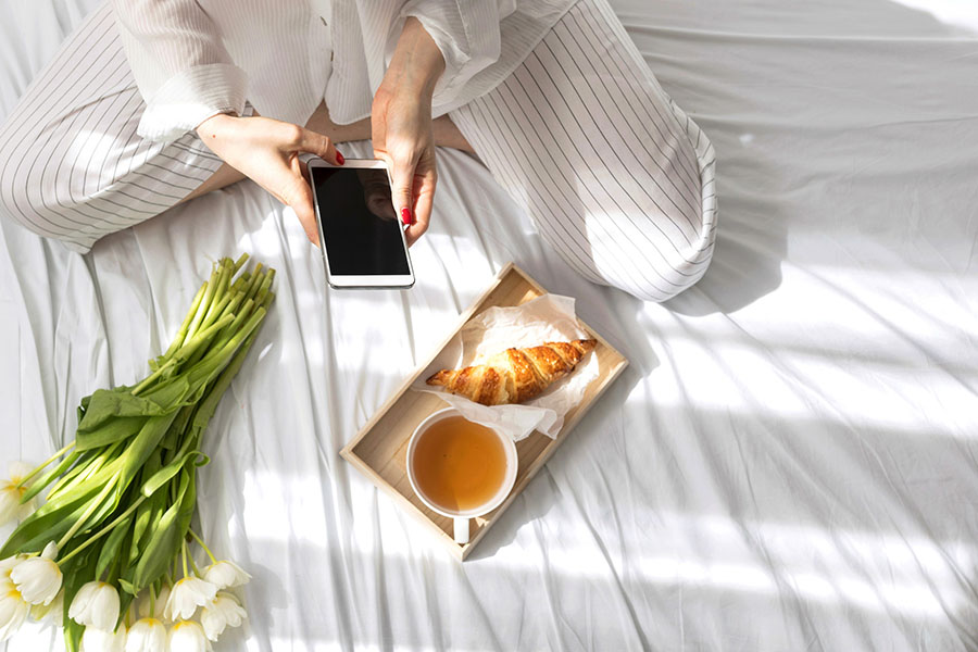 woman on bed with croissant, tea, and flowers